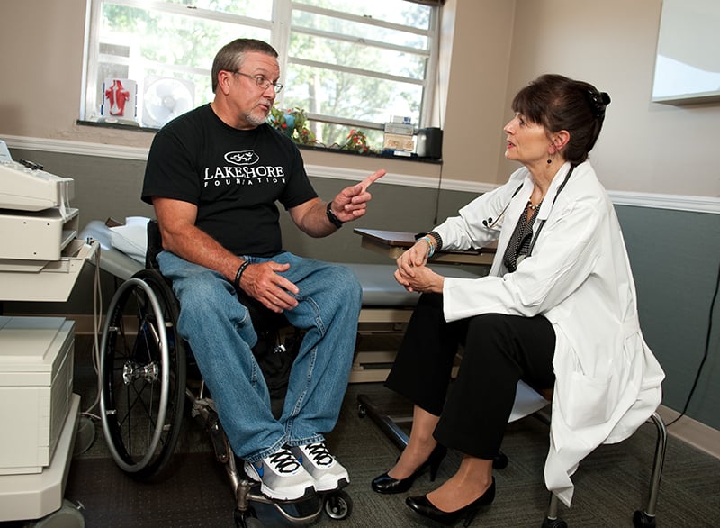 Usuario en silla de ruedas conversando con una doctora en un consultorio.