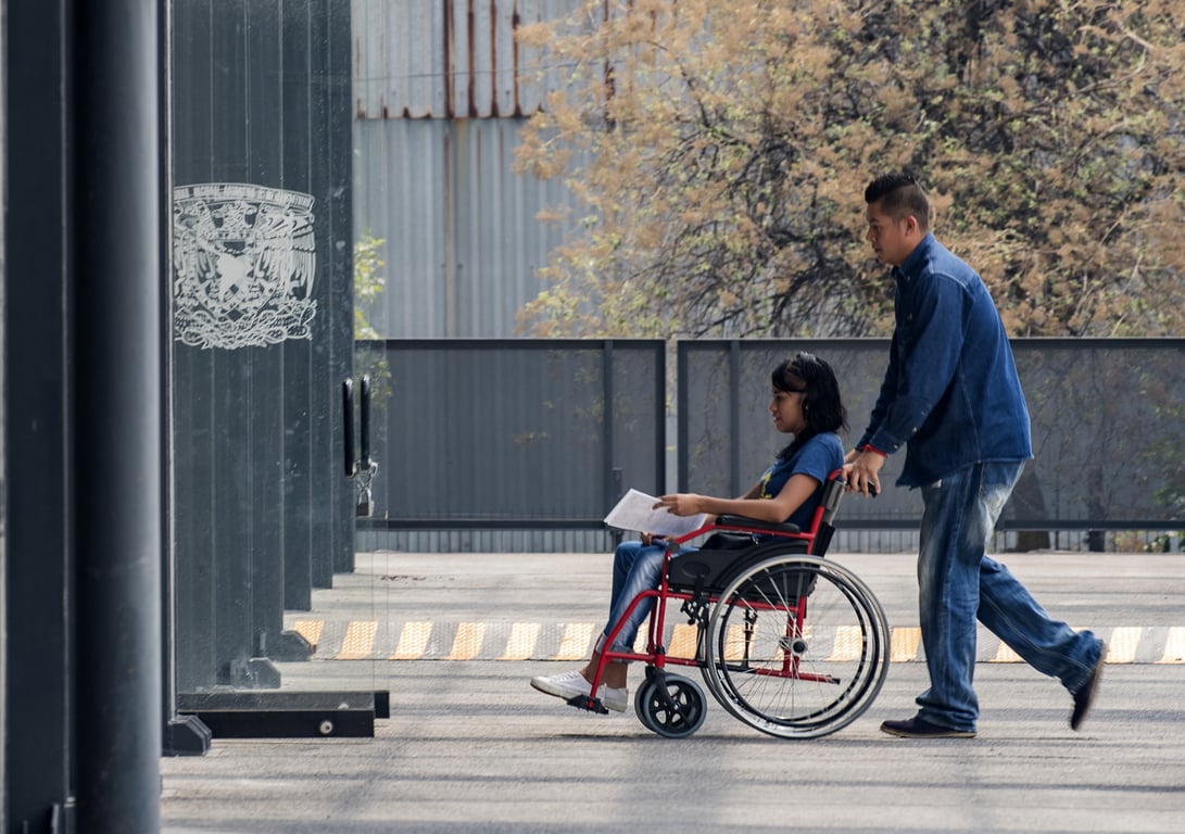 Alumna con discapacidad motriz, usuaria de silla de ruedas, entrando a un edificio de la UNAM.