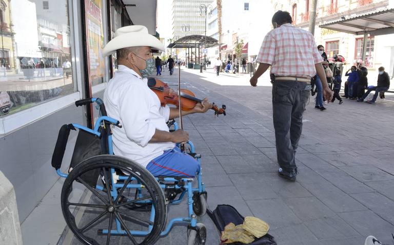 Usuario en silla de ruedas con ambas piernas amputadas tocando un violín y pidiendo dinero en la calle.