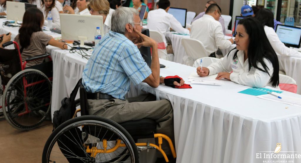 Adulto mayor usuario de silla de ruedas resolviendo una encuesta con una funcionaria pública.