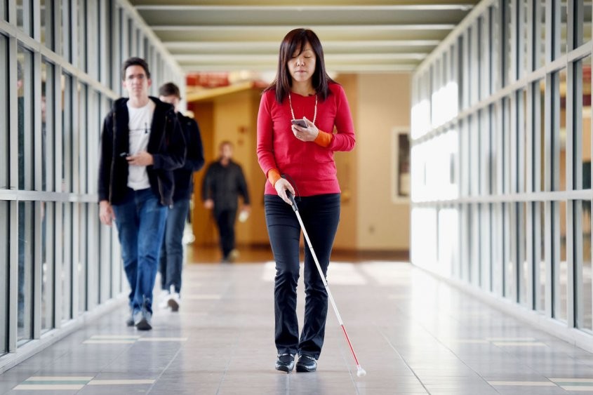 Persona ciega utilizando su teléfono celular mientras camina por un pasillo