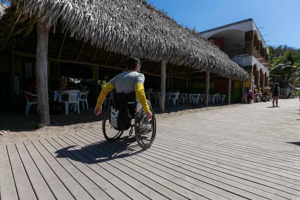 Usuario en silla de ruedas transitando por el muelle de madera accesible para personas con discapacidad motriz.