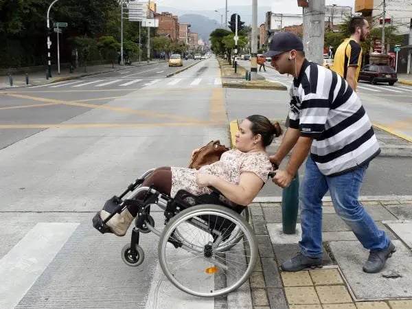 Cuidador primario y una persona usuaria de silla de ruedas cruzando con cuidado la calle.