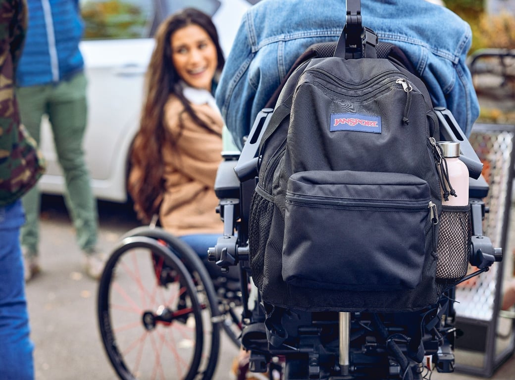 Mochila JanSport colgada en la espalda de un chico con discapacidad motriz que utiliza prótesis.