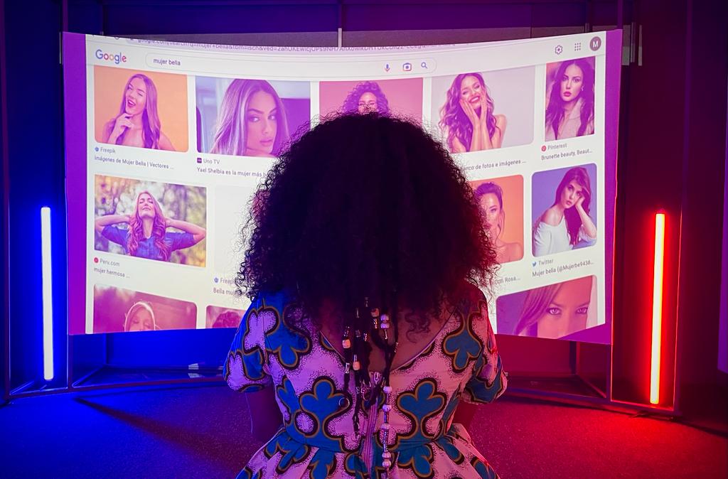Mujer frente a un monitor que tiene fotografías de diferentes mujeres.