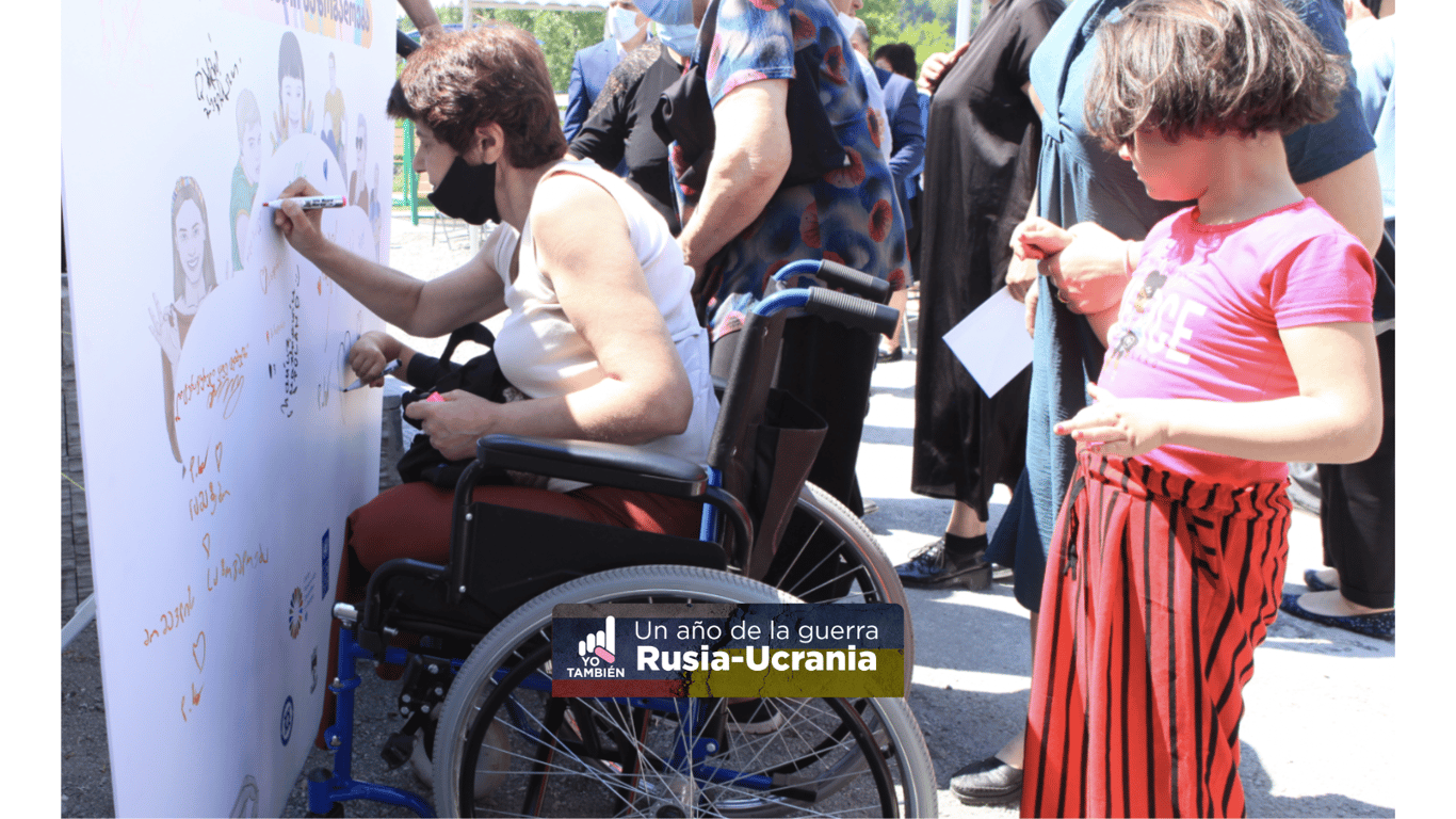Mujer usuaria de silla de ruedas firmando un muro en Georgia representativo para personas refugiadas.