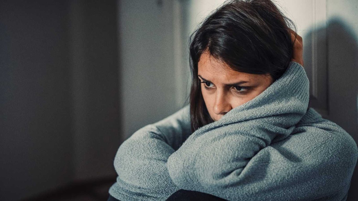 Mujer triste recargada sobre sus piernas.