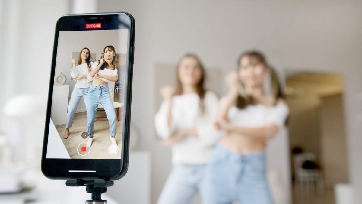 Dos adolescentes bailando frente a un teléfono celular en modo de grabación.