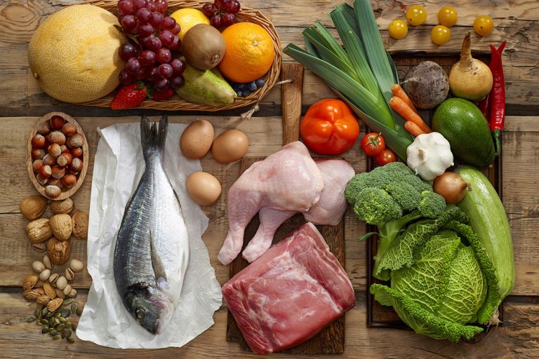 Ingredientes de la dieta mediterránea sobre una mesa: pescado, verdura, frutos secos y fruta.