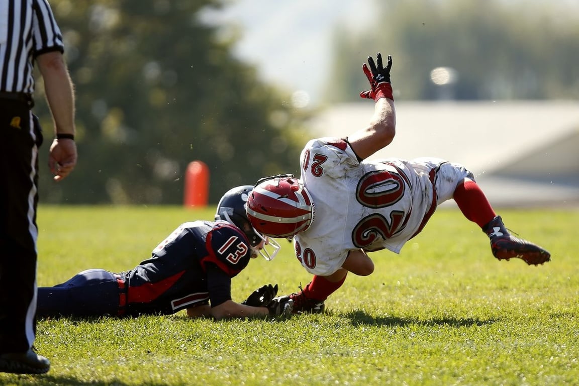 Dos jugadores de fútbol americano chocando sus cascos al caer al suelo