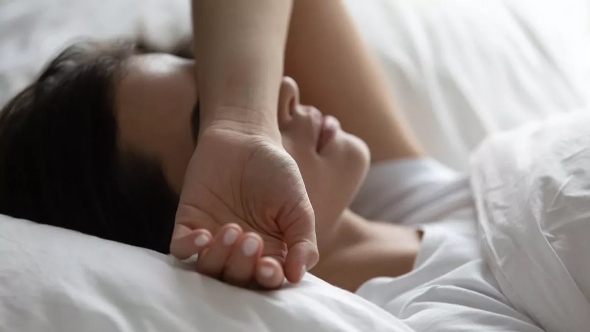 Mujer recostada en su cama con la mano sobre su rostro.