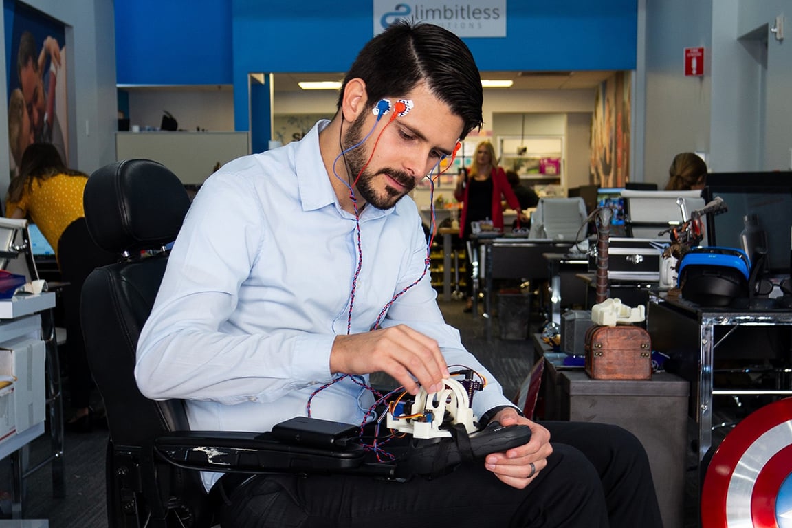 Usuario de silla de ruedas con un aparato tecnológico conectado a nodos en su cabeza y a la silla su vez.