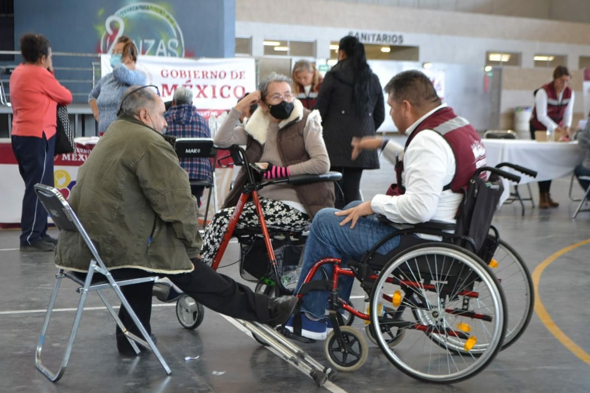 Tres usuarios en silla de ruedas platicando frente a una casilla del Gobierno de México.