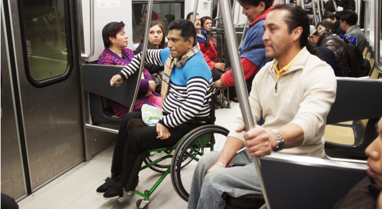 Usuario de silla de ruedas, tomando el tubo con su antebrazo para poder sostener su silla antes de descender del vagón en el metro de la CDMX