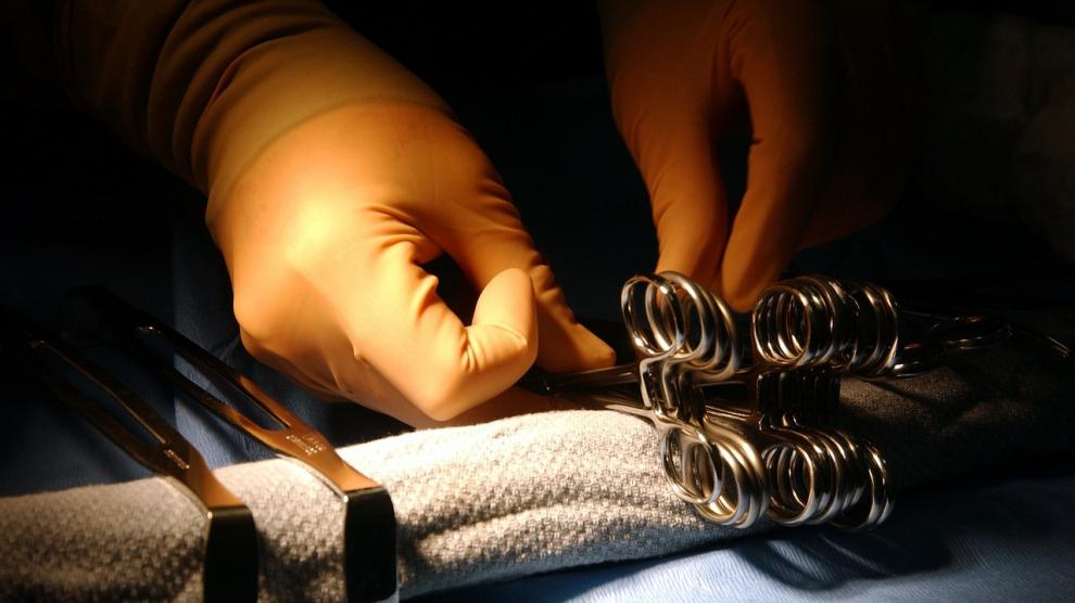 Manos con guantes quirúrgicos sosteniendo un par de pinzas dentro de un quirófano