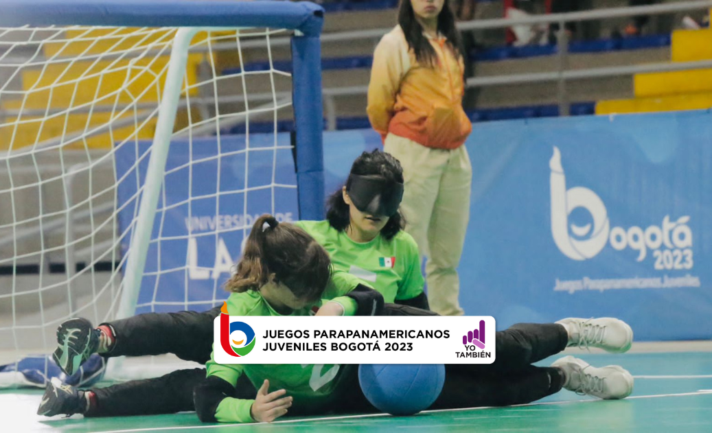 Dos mujeres del equipo mexicano se encuentran en el piso impidiendo el paso del balón hacia la portería, ambas tienen un antifaz en los ojos