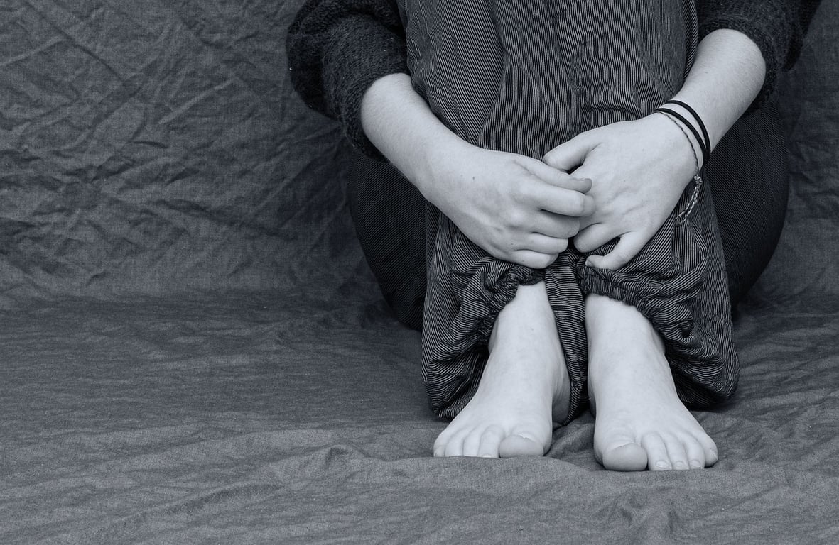 foto en blanco y negro de una mujer con problemas de salud mental sentada en el piso agarrando sus piernas