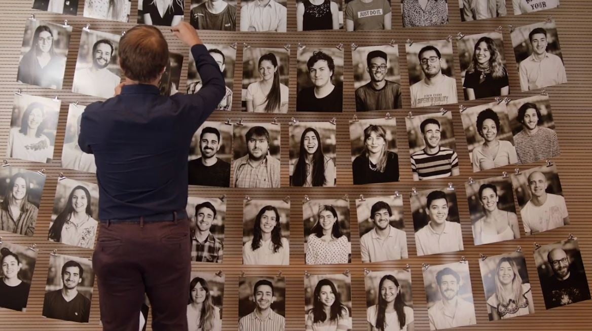 Fotografía de una persona frente a un muro lleno de fotos colocando una imagen nueva.