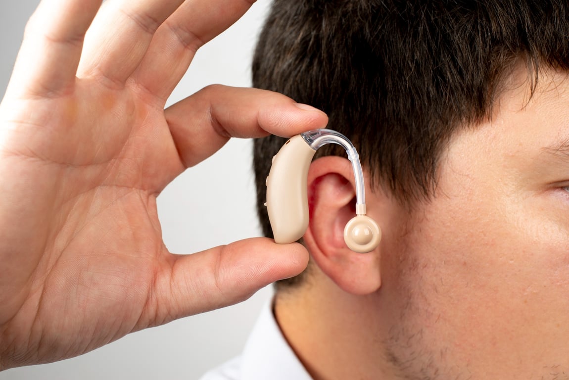Fotografía de un hombre sosteniendo un aparato auditivo frente a su oído.