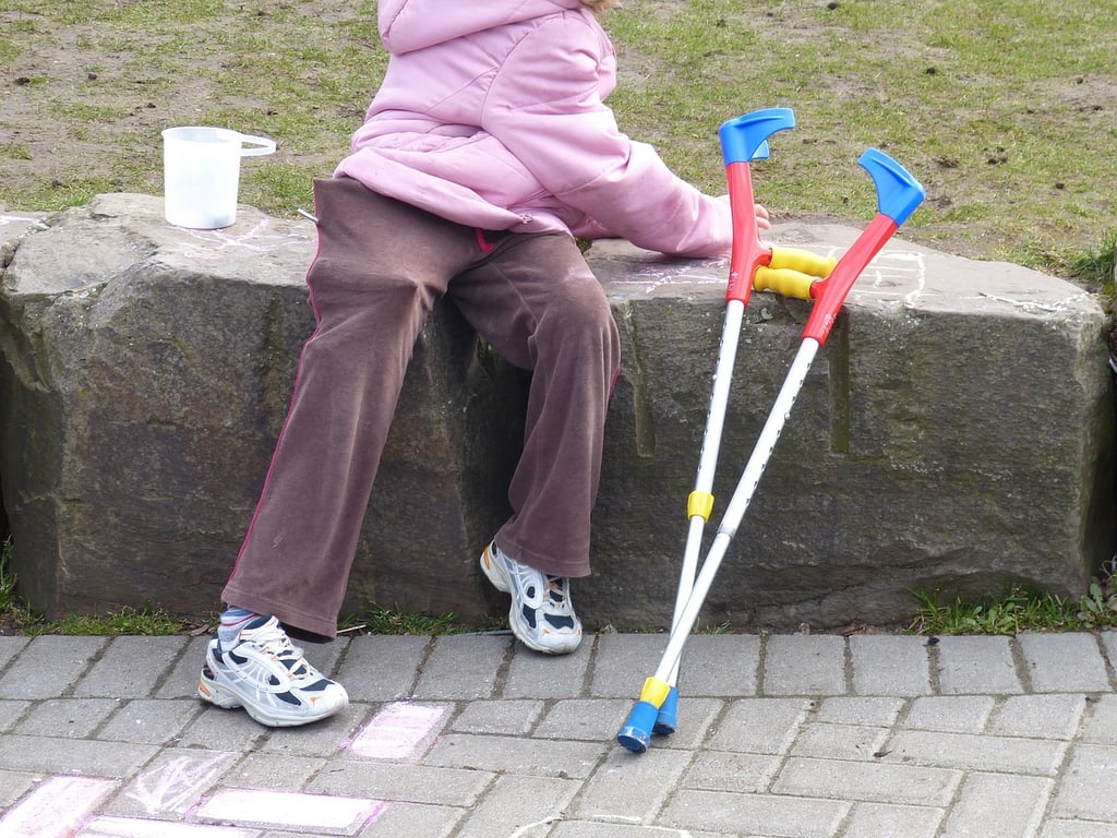 Fotografía de una niña sentada en un parque con sus muletas a un lado.