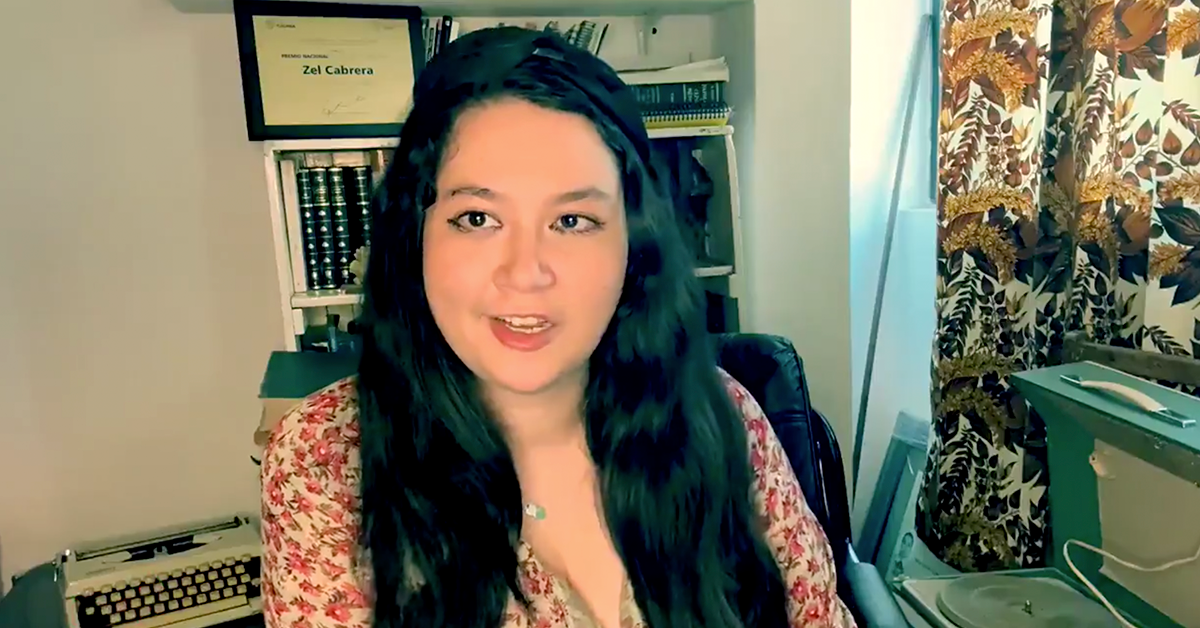 Fotografía del rostro de Zel Cabrera con el cabello suelto y una blusa color cafe, detras de ella un librero.