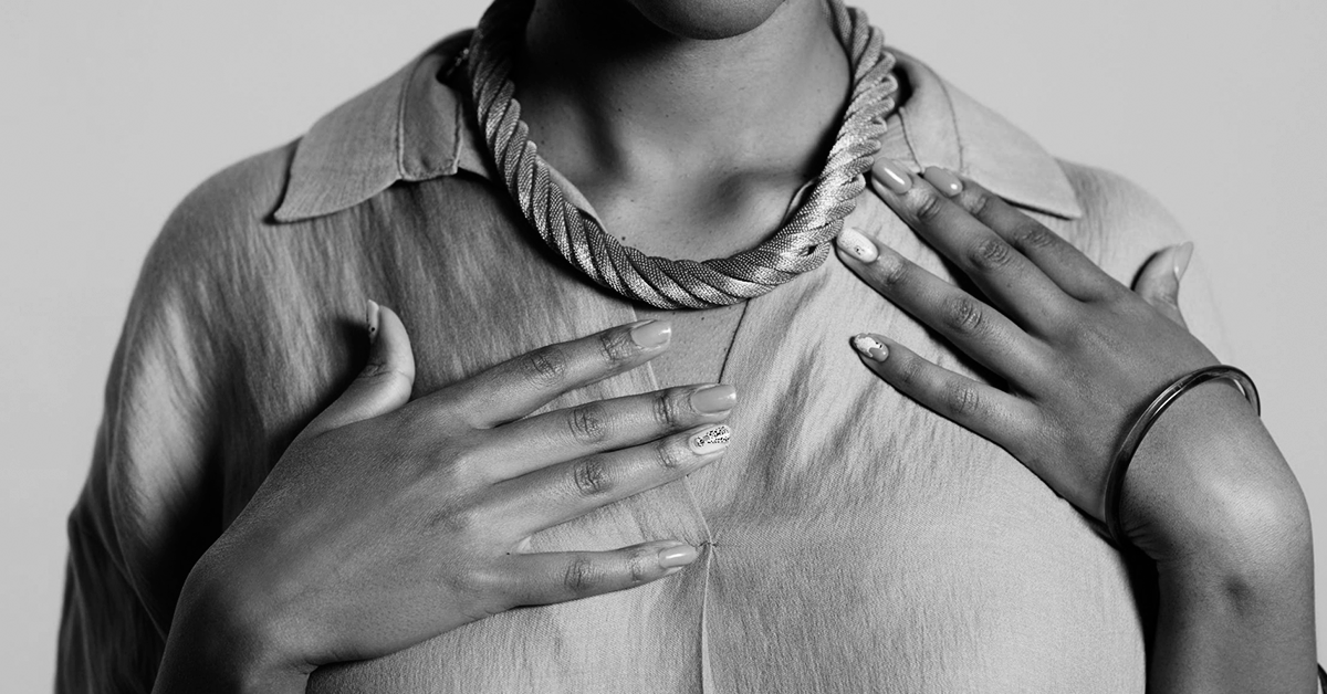 Fotografía en blanco y negro del torso de una mujer con las manos sobre su pecho.