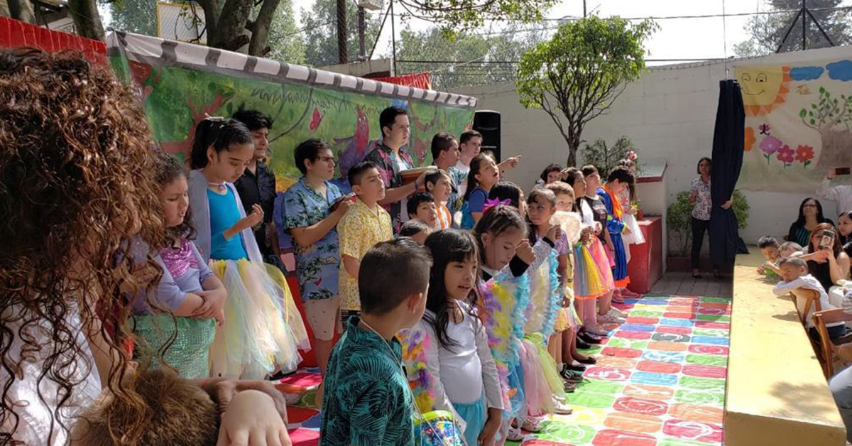 Fotografía de el patio de una escuela donde se encuentran los estudiantes disfrazados realizando una coreografía frente a los padres de familia.