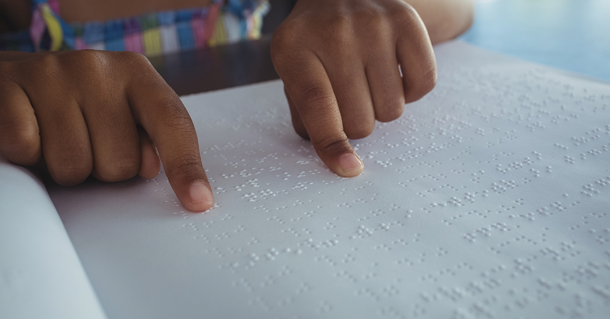 Fotografía de unas manos sobre una hoja de papel leyendo en braille