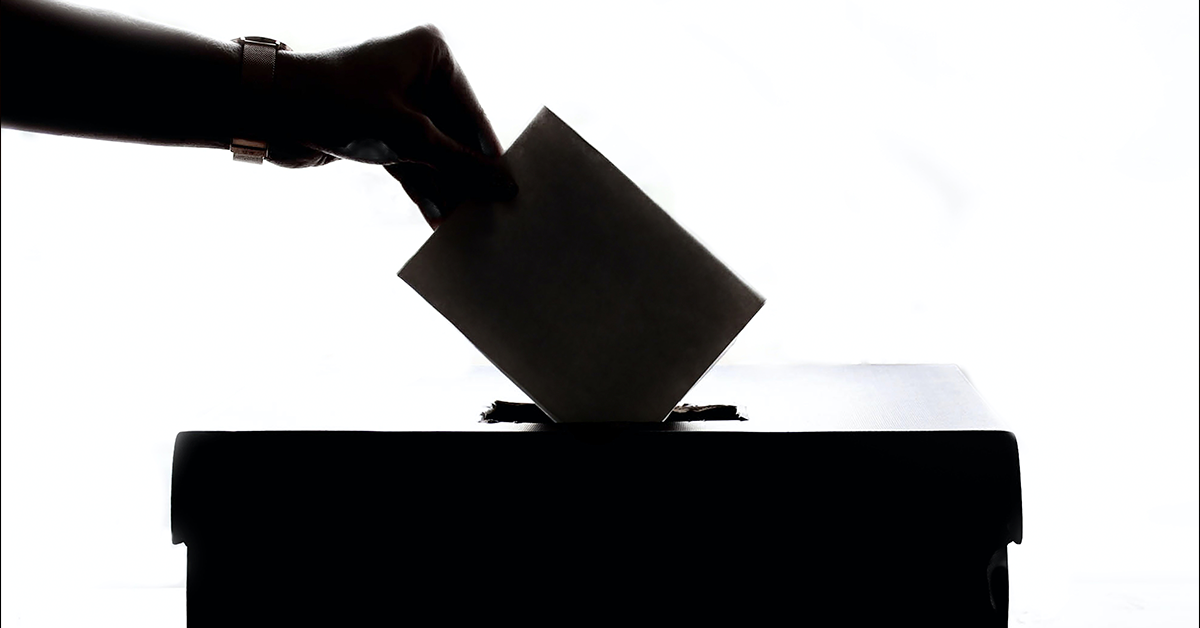 Fotografía en blanco y negro de una mano insertando una boleta electoral en una urna.