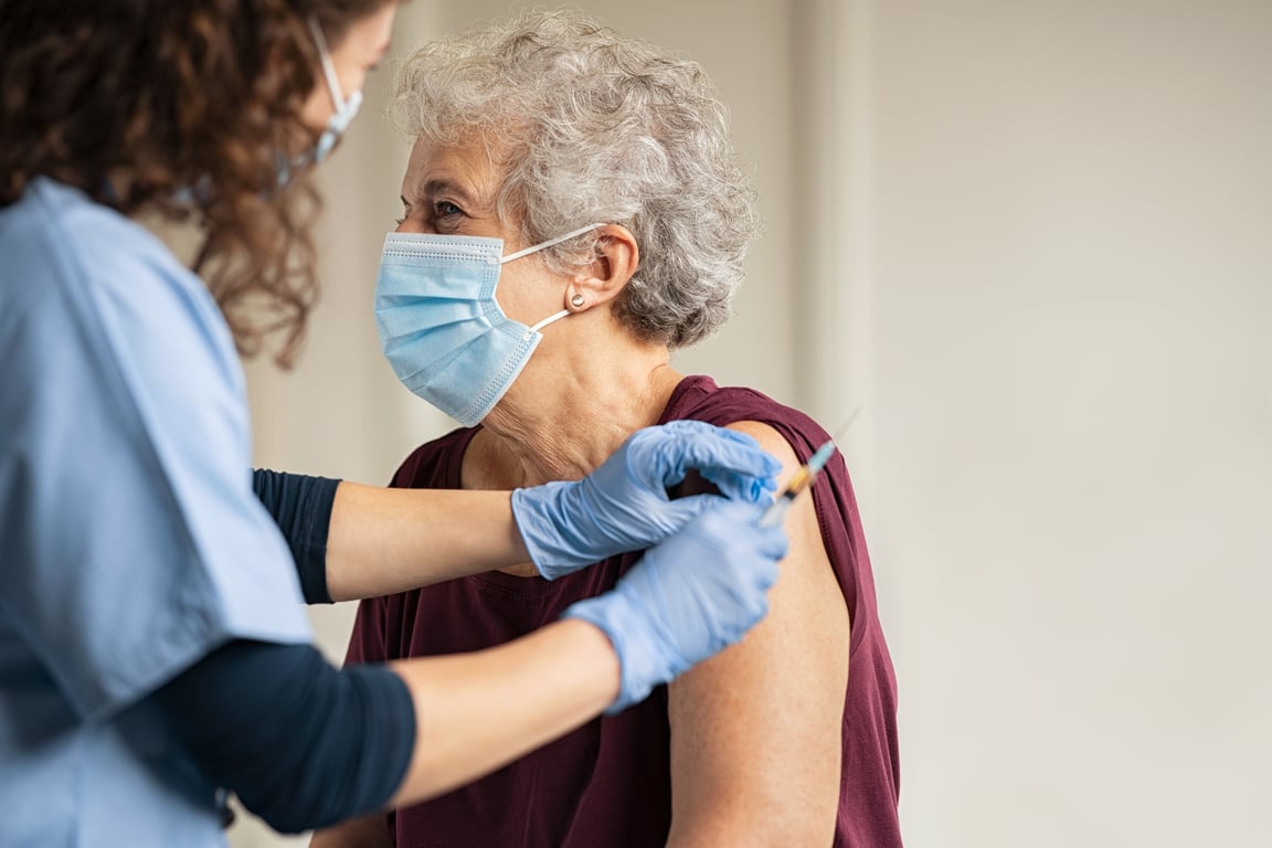 Fotografía de una mujer adulta con cubrebocas siendo vacunada en el brazo por una enfermera.