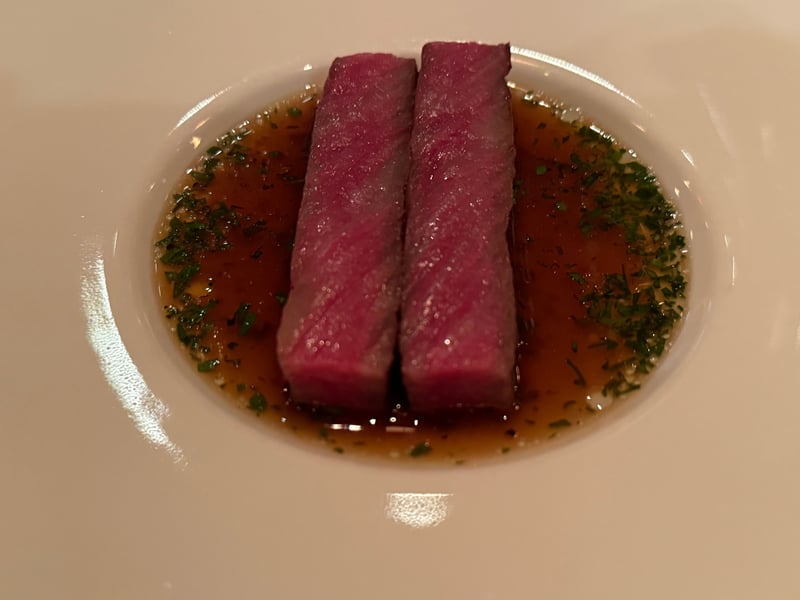 褐色のコンソメに、桃色の牛肉を2本並べる。刻んだ緑を散らす