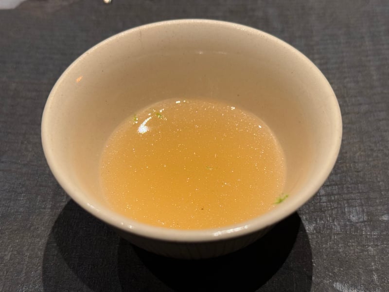 白い小椀に注がれた明石鯛のエッセンス。澄んだ琥珀色