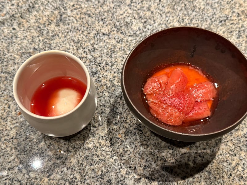 赤い液に白い塊を沈めた小さな器と、苺を並べた黒い椀