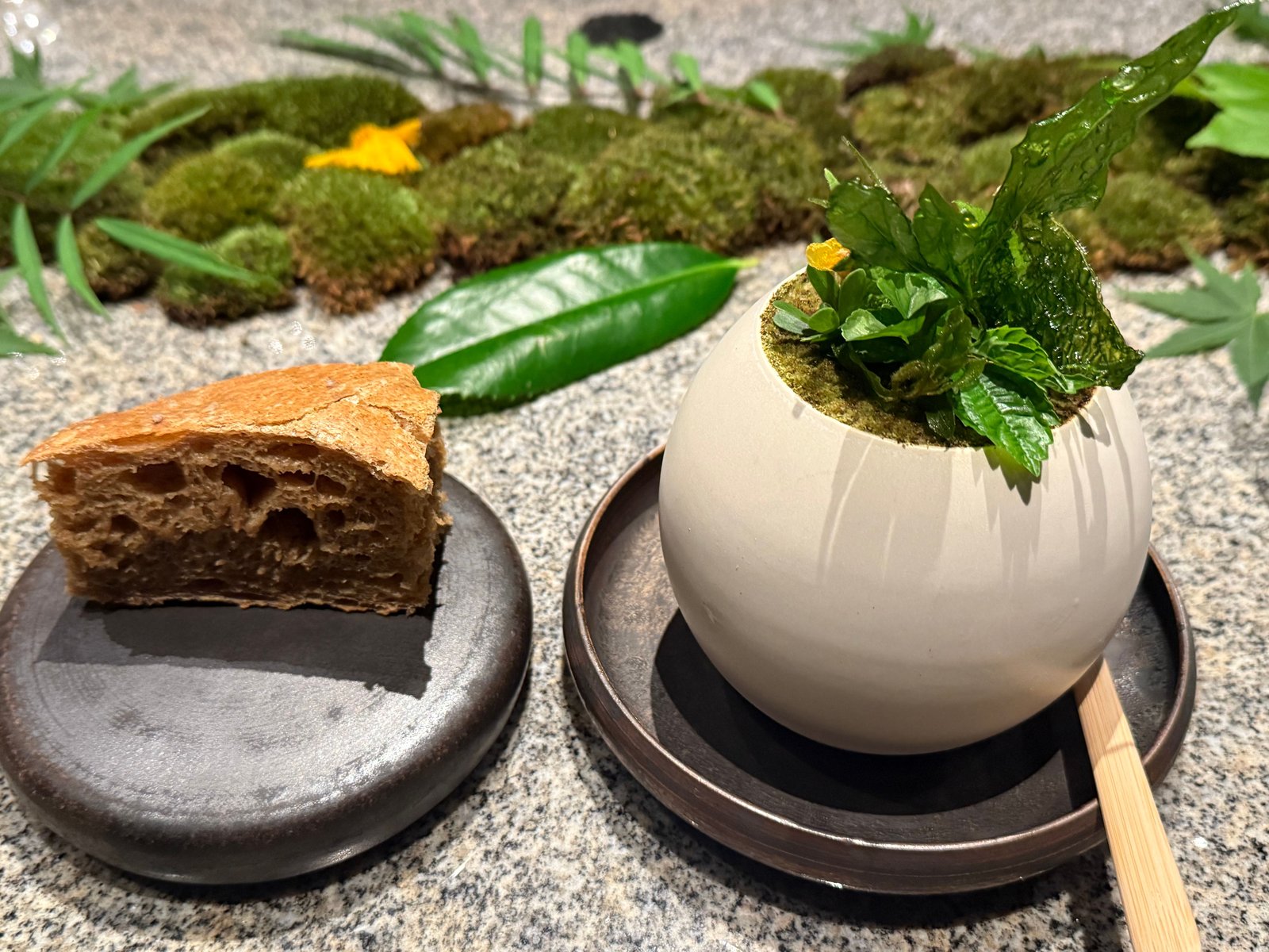 始末のパンと、山野草を生けた白い球形の器。苔の上に置かれている
