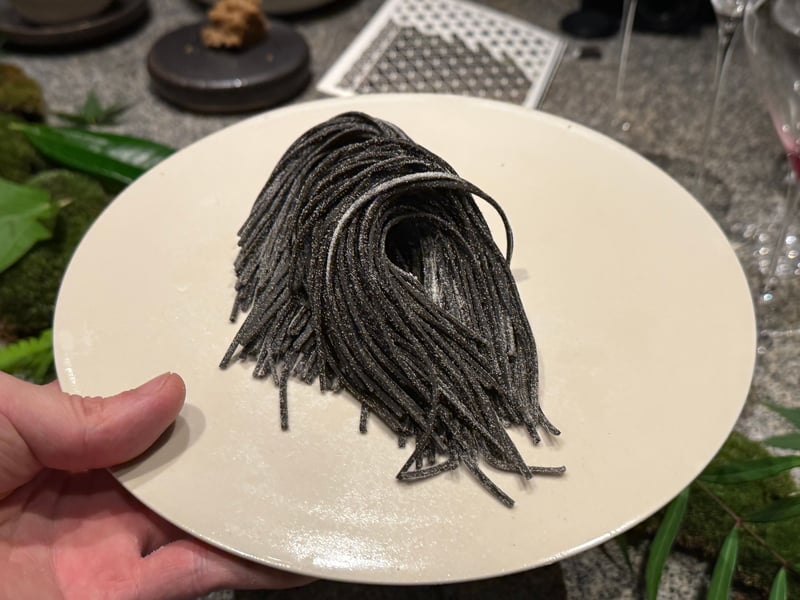 イカスミを打ち込んだ黒い自家製麺を束のまま皿にのせて見せているところ