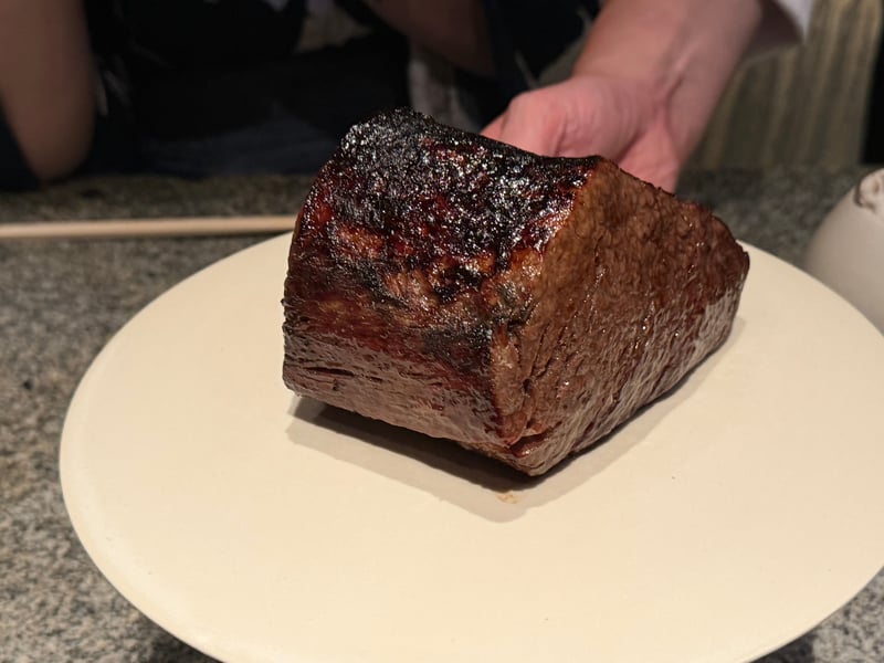 表面を焼いた近江牛の塊を皿にのせて卓に見せているところ
