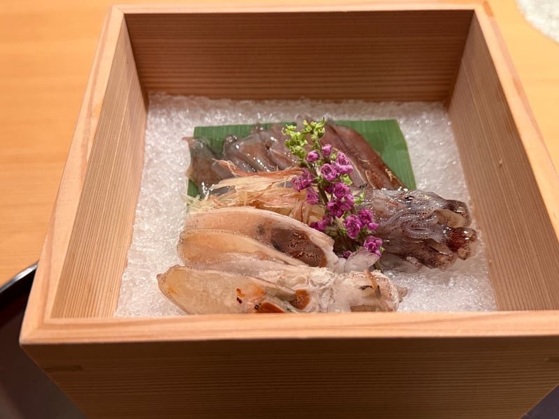 木箱の氷の上に、ホタルイカの刺身とルイベ。桜色の小花を添えて