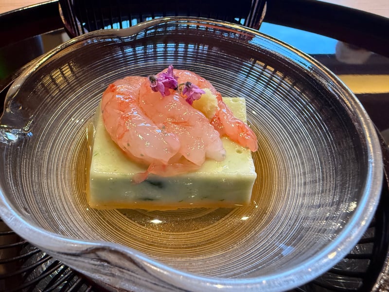 ガラスの器に入ったよもぎ豆腐と、その上にのせた甘海老と紫の花