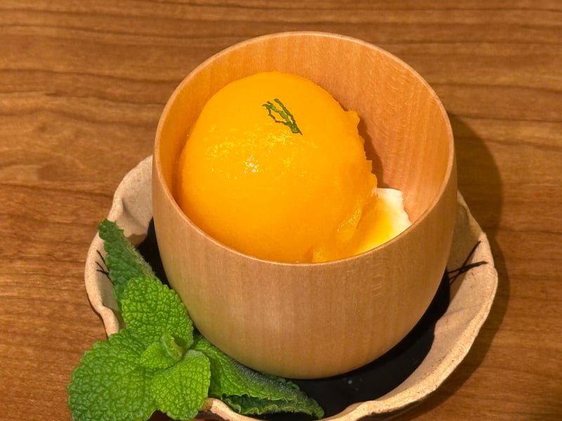 木のカップに橙色のソルベ、下に豆乳の杏仁豆腐