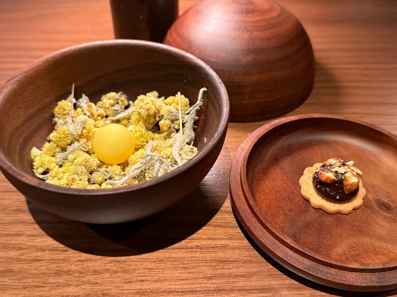 乾いた黄色い花を敷いた器に球がひとつ。木皿にチョコレートとナッツのクラッカー