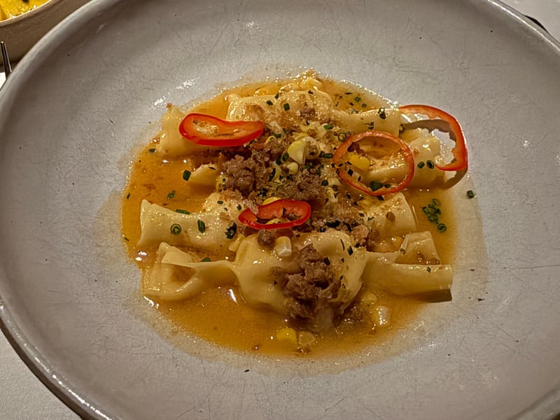 橙色の出汁にパスタの包み。チョリソーのそぼろ、とうもろこしの粒、赤唐辛子の輪切り