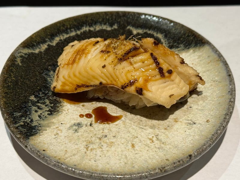 灰釉の皿にのった、ツメを塗った穴子の握り。焼き目に山椒が振ってある。