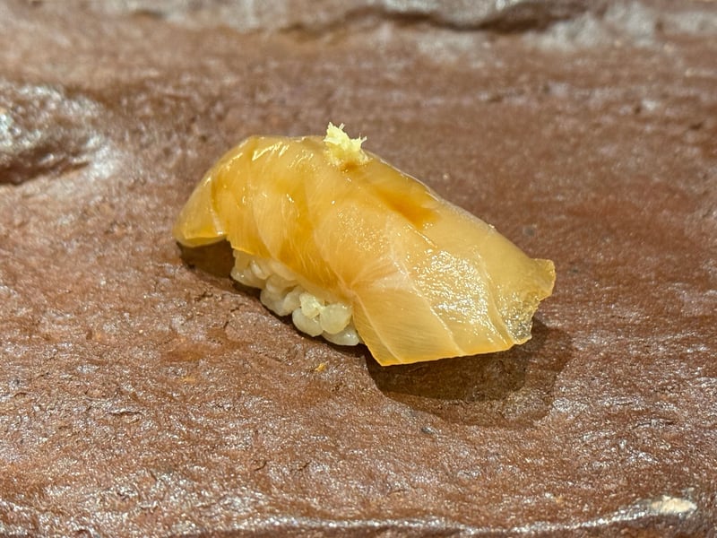 茶色い石の台にのった、飴色に漬けたシマアジの握り。上におろし生姜。