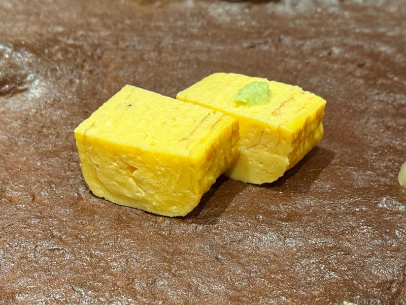 茶色い石の台にのった、二切れに切った玉子焼きとわさび。
