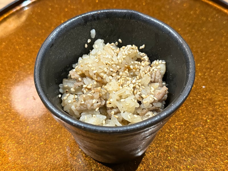 黒い筒形の器に盛った牛蒡と肉の炊き込みご飯、白胡麻