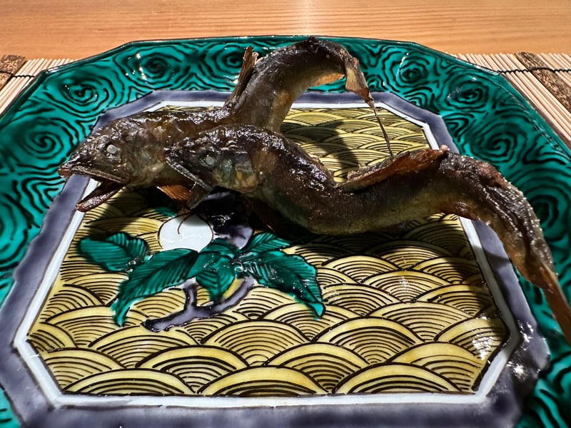 緑の角皿に炭火で焼いた天然鮎が二尾、泳ぐような形に盛られている