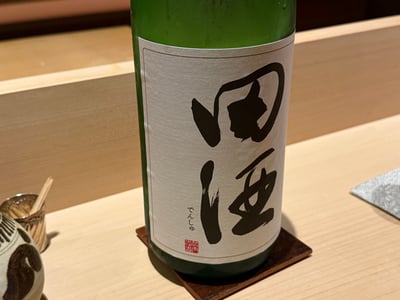 檜のカウンターに置いた田酒の一升瓶。白いラベルに墨書き。