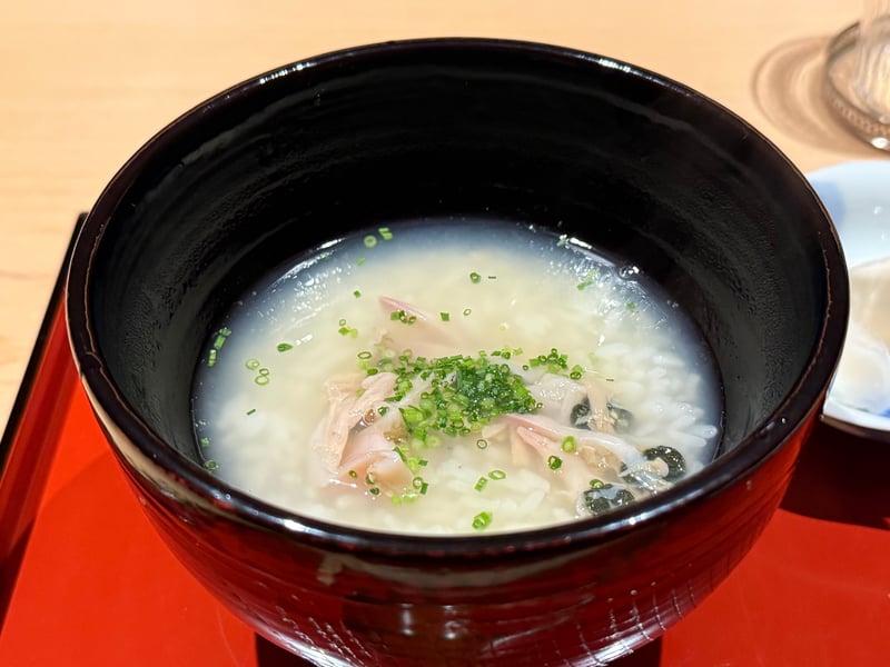 黒漆の椀に蛤の雑炊。身と小口葱がのっている。