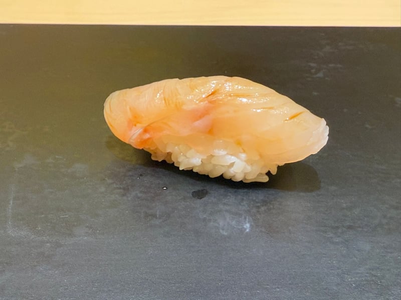 黒いつけ台に、淡い白身のアラの握り
