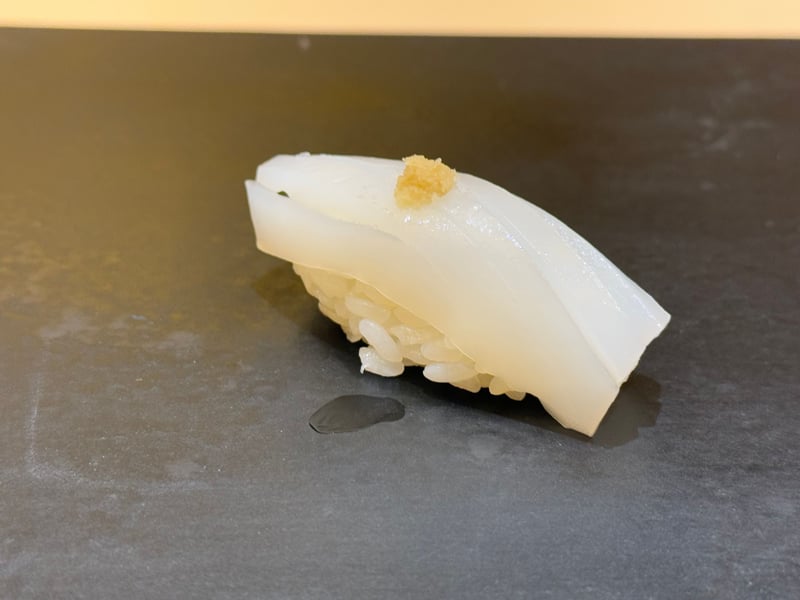 黒いつけ台に、白いコウイカの握り。生姜をひとつまみのせて
